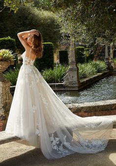 a woman in a white wedding dress standing on the side of a stone wall with her back to the camera