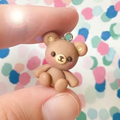 a tiny brown teddy bear sitting on top of a persons finger in front of a polka dot wall