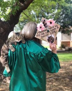 a woman holding a cat in her arms while wearing a green graduation gown with flowers on it