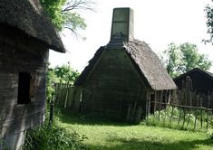 an old wooden house with a thatched roof in the middle of a grassy field