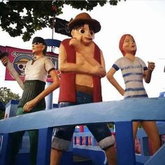 statues of three men standing on top of a blue structure with trees in the background