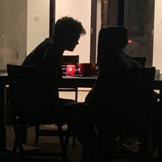 two people sitting at a table in front of a window with a red light on it