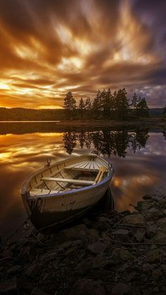 a small boat sitting on top of a lake next to a shore covered in rocks