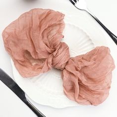 a white plate topped with a pink scrunch on top of a table next to utensils