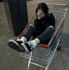 a person sitting in a shopping cart with their feet on the ground and one hand over their face