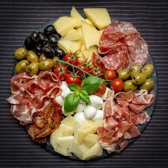 an assortment of cheeses, meats and olives arranged in a circle on a plate