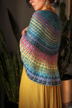 a woman wearing a multicolored shawl in front of a potted plant