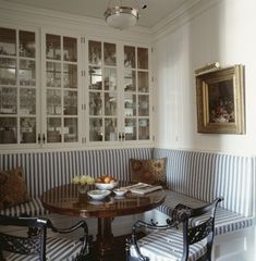 two chairs and a table in a room with striped upholstered bench, framed pictures on the wall