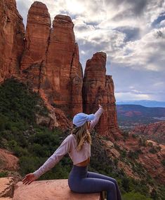 a woman sitting on top of a rock formation with her arms outstretched in the air