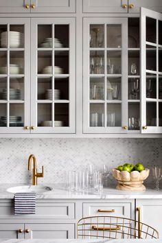 a kitchen with white cabinets and gold handles, marble countertops and glass front cupboards