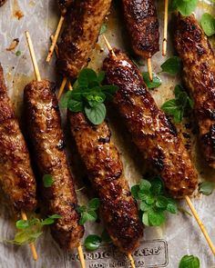 several skewers of meat with toothpicks and herbs on them sitting on a piece of parchment paper