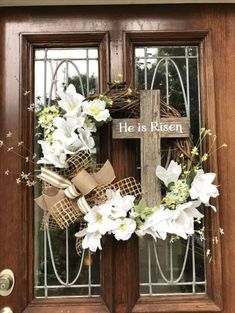 a wreath with flowers and a cross on it is hanging on the front door of a house