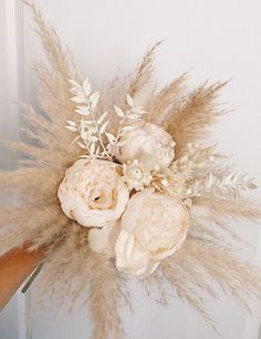 a bouquet of white flowers and feathers on a doorknob with someone's hand holding it