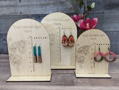 three wooden earrings and earring holders on display with flowers in the backgroud