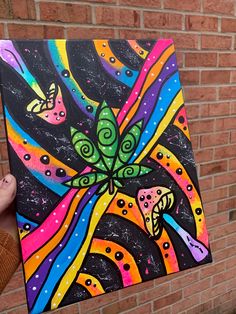 a person holding up a colorful painting in front of a brick wall with butterflies on it