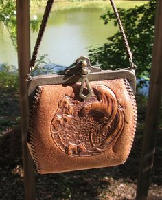 "Love this little antique handbag! The metal frame has some discoloration, and there are a couple of small areas of stitch loss on the strap, but this is otherwise in pretty remarkable condition for the age! The front circular design is a bird with long feathers and a prominent beak on a branch with what looks to be ivy on the other side. The inside is an antique green suede, with a sleeve pocket on each side. This has a button clasp with the metal charm hanging down, I took a picture of the back side of the charm, the only identifying mark I could find anywhere. The main body of the purse measures 5 & 1/2\" from top to bottom and 5 & 1/4\" across. The strap drop is 5 & 1/2\".  Great early western leather handbag!" Vintage Handheld Handmade Bag, Handmade Vintage Handheld Shoulder Bag, Vintage Handmade Rectangular Shoulder Bag, Handmade Vintage Rectangular Shoulder Bag, Antique Engraved Rectangular Bag, Antique Engraved Rectangular Bags, Antique Rectangular Engraved Bags, Vintage Hand-tooled Shoulder Bag Gift, Vintage Hand Tooled Shoulder Bag Gift