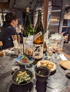 a table topped with plates and bowls filled with food next to two bottles of wine