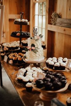 a table filled with cakes and cupcakes on top of wooden tables covered in frosting