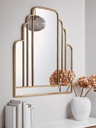 a white vase with flowers in front of a gold framed mirror on a shelf next to a bookcase