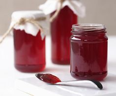 two jars filled with red liquid sitting on top of a white table next to a spoon