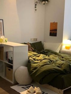 a bed with green sheets and pillows in a room next to a white table lamp