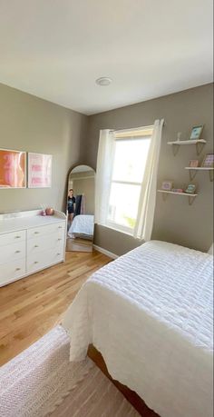 a white bed sitting next to a window in a bedroom on top of a hard wood floor