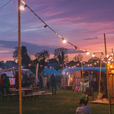 a group of people standing in front of tents with lights strung from them at dusk