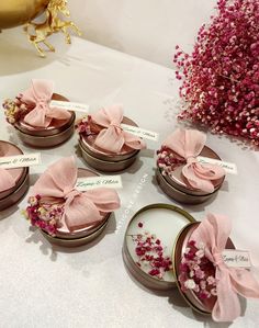 six small round boxes with pink bows on them sitting on a table next to flowers