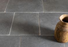 a brown vase sitting on top of a stone floor next to a black tile floor