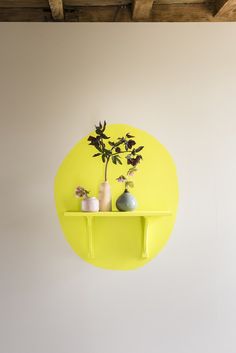 a yellow shelf with two vases and a plant on it in front of a white wall