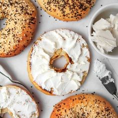 four bagels with cream cheese and sprinkles on them next to two small bowls