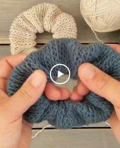 two hands holding up a blue knitted object in front of yarn balls on a wooden surface