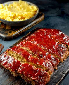 meatloaf with ketchup and mashed potatoes on a cutting board next to it