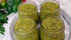 four mason jars filled with pesto sauce sitting on a white plate next to green peppers