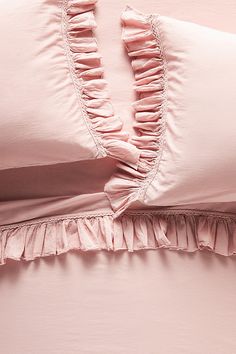 a pink comforter with ruffled edges and pillow cases on a light pink bed