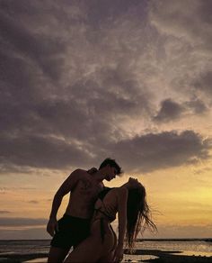 a man and woman are standing on the beach at sunset with their backs to each other