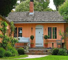 an orange house with a white door and steps leading up to the front door is surrounded by greenery