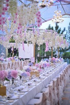 a long table covered in lots of white and pink flowers with chandeliers hanging from the ceiling