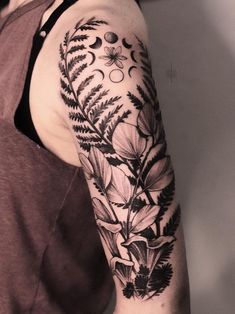 a black and white photo of a woman's arm with flowers, leaves and moon tattoos on it