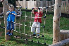 two young boys are playing on a rope course in the yard with their hands together