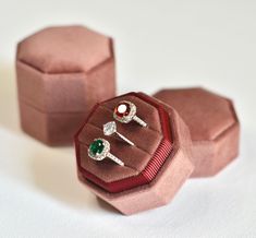 two rings are sitting in a pink velvet ring box on a white surface with other jewelry items