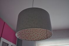 a lamp shade hanging from the ceiling in a room with pink walls and white curtains