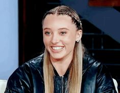 a woman with long hair wearing a black jacket and smiling at the camera while sitting down