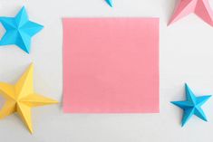 three paper stars next to a pink square and two blue ones on a white surface