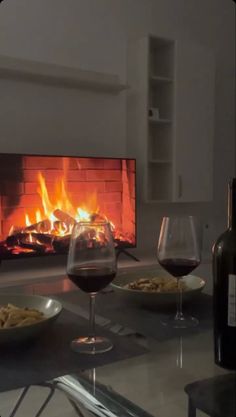 two glasses of wine are sitting on a table in front of an open fire place