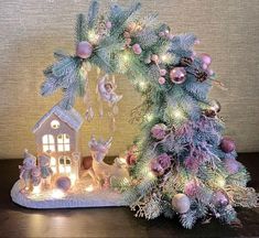 a small christmas tree with lights and ornaments on it next to a lit up house