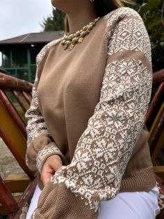 a woman sitting on a wooden bench wearing a brown sweater and white pants with lace sleeves