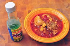 a bowl of stew next to a bottle of hot sauce