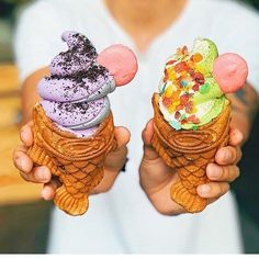 two people holding up ice cream cones with mickey mouse ears on their heads and colorful toppings