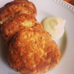 three crab cakes on a white plate with a dollop of mayonnaise next to it